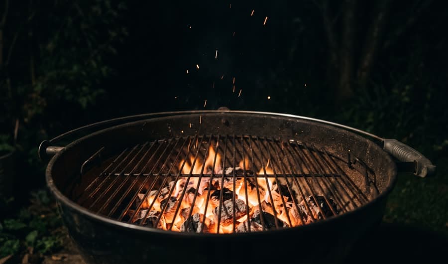 Glowing charcoal embers and low flame in an outdoor grill at night