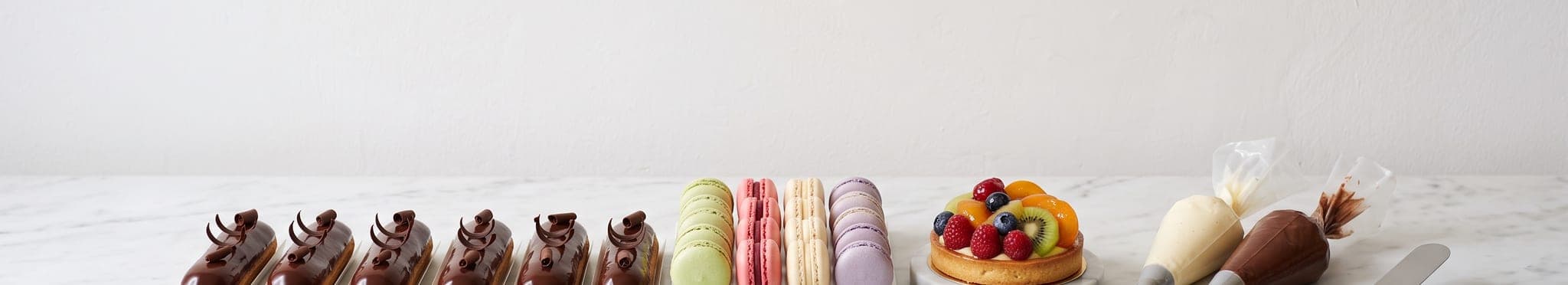 A row of éclairs, macarons and a glazed tart on a pale marble counter